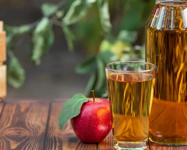 Manzana roja junto a un vaso y botella de vinagre de manzana para limpiar. Cosecha fresca en caja de madera al fondo.